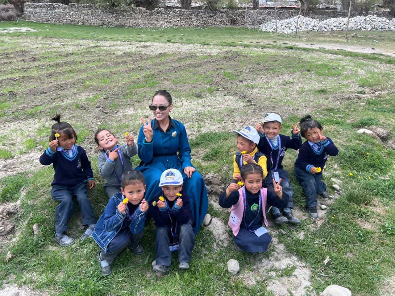 Primary students holding wildflowers with their teacher on the grass outside the school