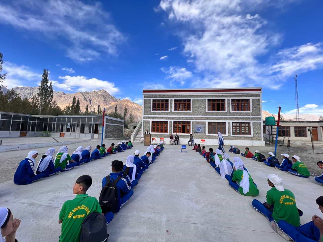 Students of Govt. Model Higher Secondary School Partapur seated in the school courtyard with the Nubra mountains behind